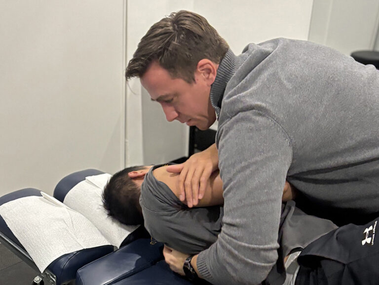 A male chiropractor performing a manual spinal adjustment on a patient lying on a treatment table.