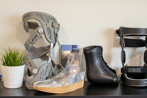 A display of medical orthopedic devices including rigid knee braces, custom foot orthotic molds, and supportive footwear.