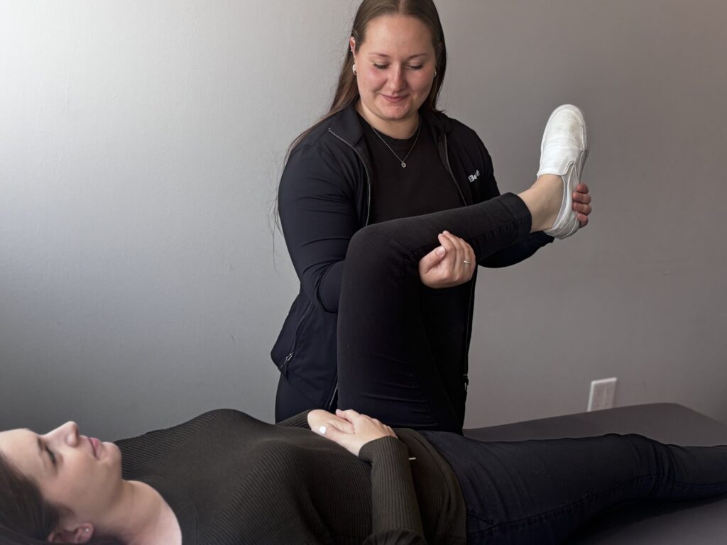 A female clinician gently guiding a patient's leg through a hip and knee mobility stretch on a treatment table.