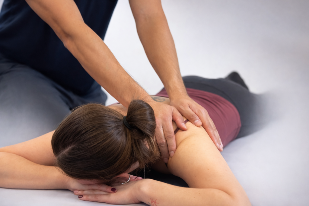 A therapist applying targeted pressure to a patient's upper back and shoulder muscles during a massage session.